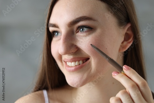 Smiling woman drawing freckles with pen indoors  closeup