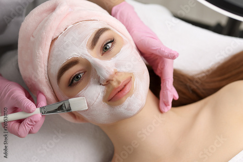 Cosmetologist applying mask on woman's face, top view