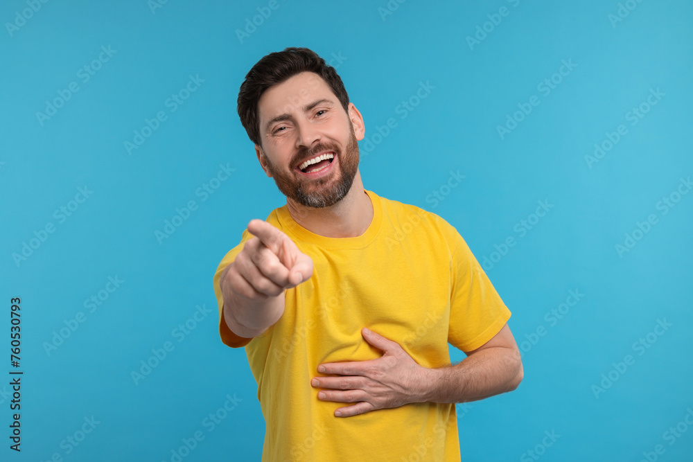 Handsome man pointing at something and laughing on light blue background Handsome man pointing at something and laughing on light blue background