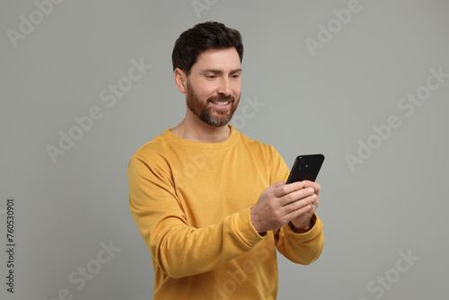 Smiling man with smartphone on grey background © New Africa