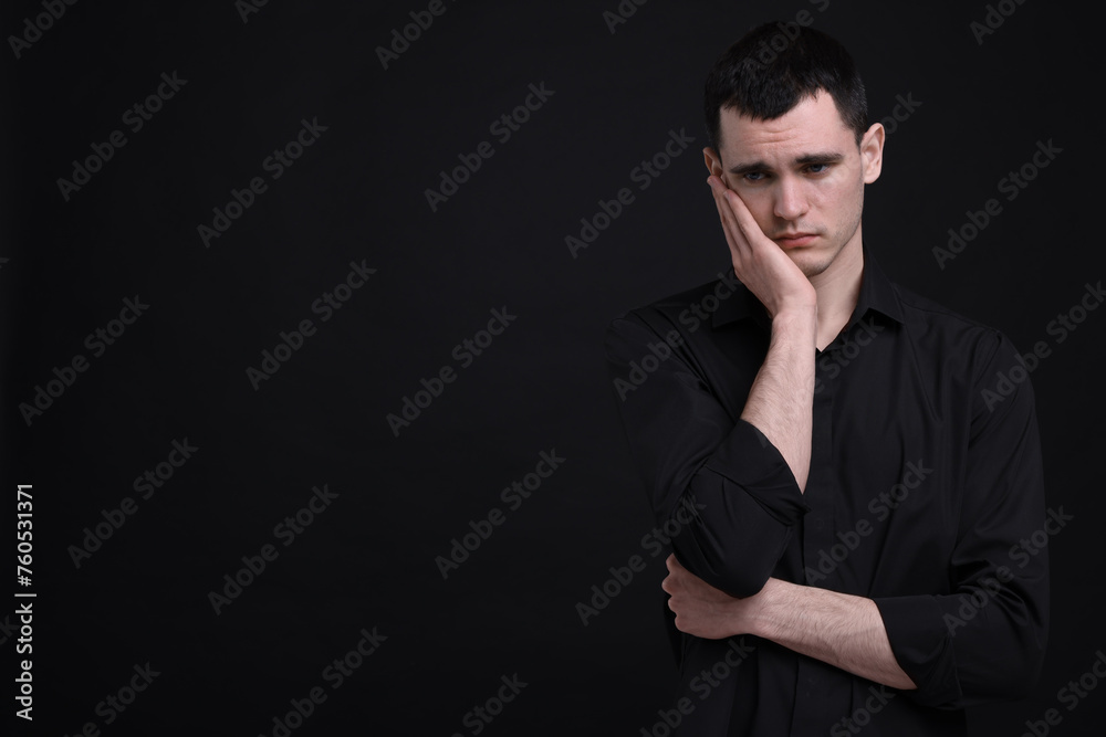 Portrait of sad man on black background, space for text