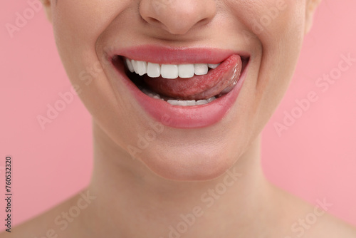 Young woman licking her teeth on pink background  closeup