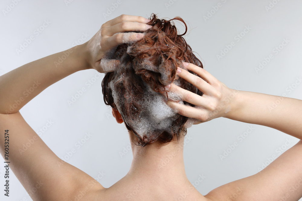 Young woman washing her hair with shampoo on light grey background, back view Young woman washing her hair with shampoo on light grey background, back view
