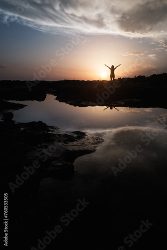 woman on sea shore at sunset raising arms
