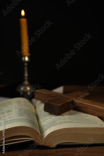 Church candle, Bible and cross on wooden table against black background