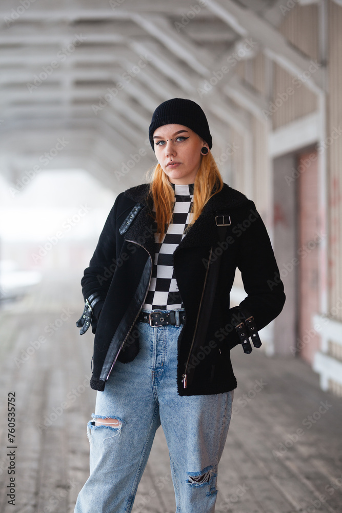 Fototapeta premium Edgy female model with piercings, beanie and blond hair. Dark tones and blurry background