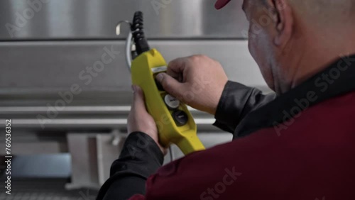 Professional winery worker operates an automated production facility with buttons on a lisping control panel in his hands.  photo