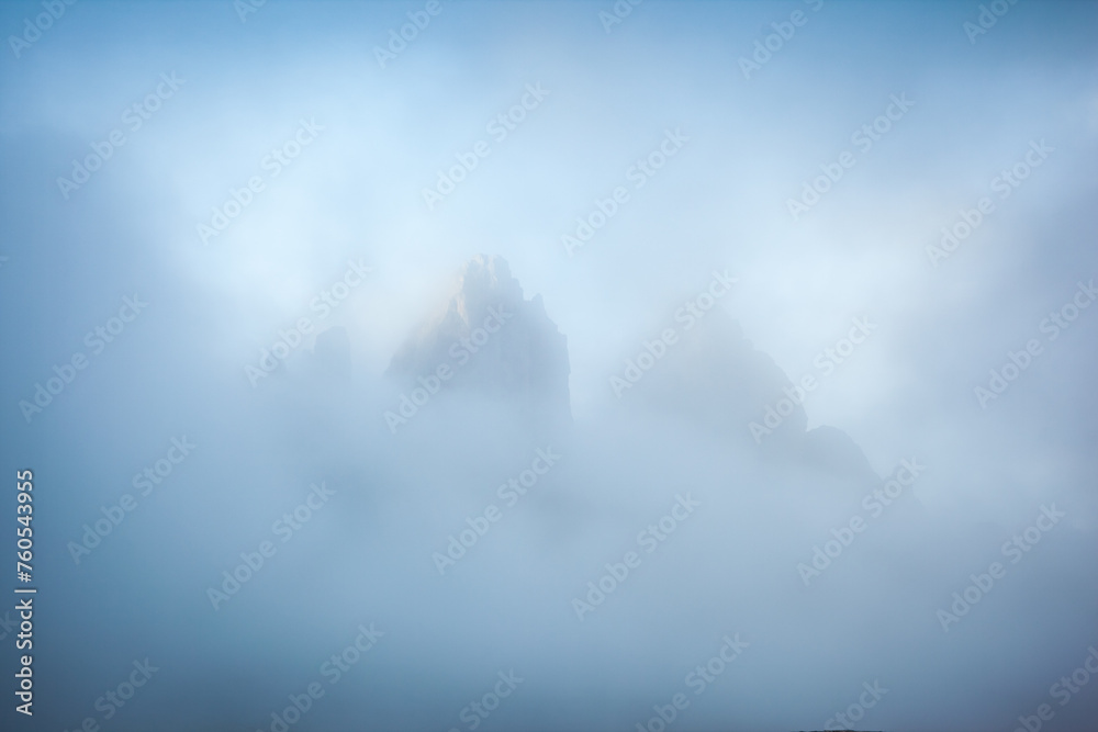 The sharp peaks of Tre Cime di Lavaredo are visible through the mist. Sexten Dolomiti, South Tyrol, Europe. - obrazy, fototapety, plakaty 
