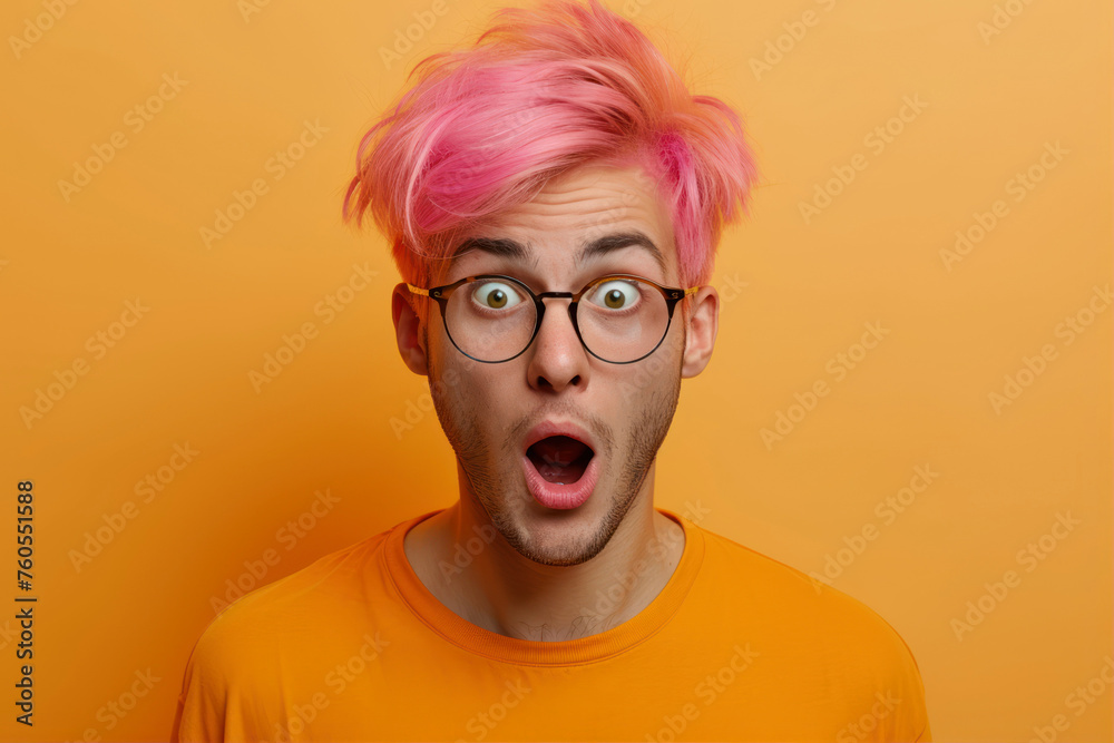 Surprised young man with pink hair and glasses on orange background