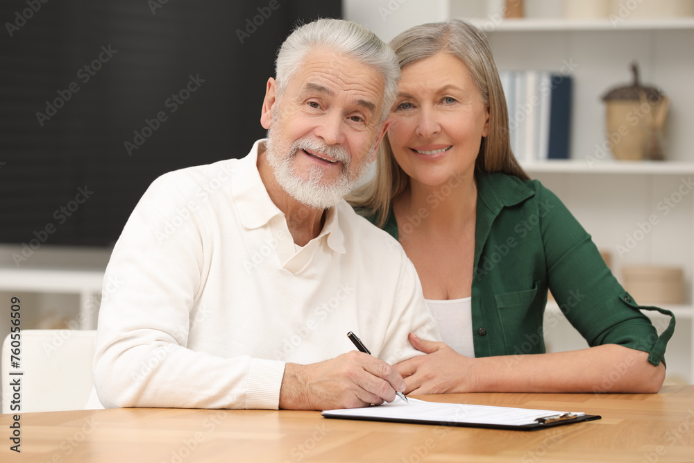 Happy senior couple signing Last Will and Testament indoors Happy senior couple signing Last Will and Testament indoors