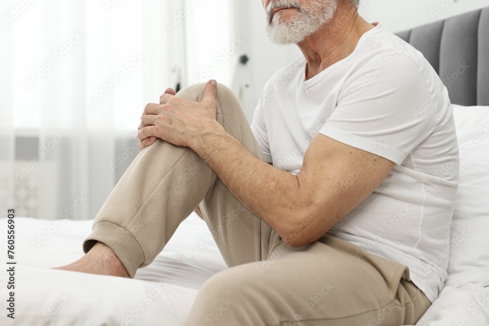 Arthritis symptoms. Man suffering from pain in knee on bed at home Arthritis symptoms. Man suffering from pain in knee on bed at home