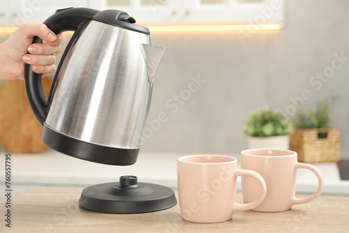Woman with electric kettle in kitchen, closeup. Space for text
