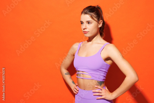 Side profile view young fitness trainer instructor sporty woman sportsman wear purple top clothes spend time in home gym stand akimbo isolated on plain orange background Workout sport fit abs concept