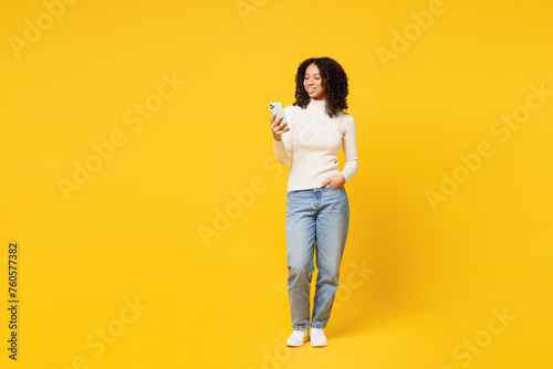 Full body happy little kid teen girl of African American ethnicity wear white casual clothes hold in hand use mobile cell phone isolated on plain yellow background studio. Childhood lifestyle concept.