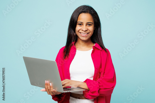 Little kid teen IT girl of African American ethnicity wear pink shirt white t-shirt hold use work on laptop pc computer isolated on plain pastel light blue cyan background Childhood lifestyle concept