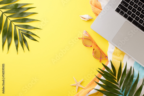 Tropical telecommuting setup. Overhead view of palm leaves, beach towel, pink sunglasses, starfish, seashells and laptop on bright yellow background with space for advertising photo