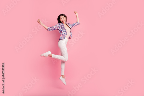 Full length side profile body size photo funny beautiful her she lady jump high holiday fists raised wear shoes casual checkered plaid shirt white jeans denim clothes outfit isolated pink background