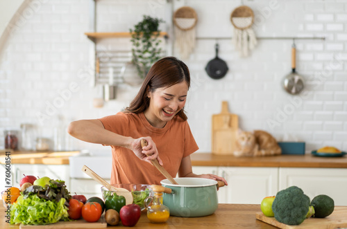 Young woman standing near stove and cooking, housewife, meal, chef, food.Happy woman looking and smelling tasting fresh delicious from soup in a pot with steam at white interior kitchen © Art_Photo