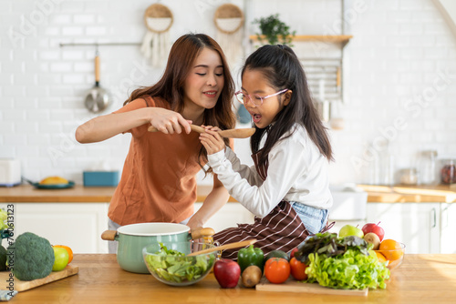 Portrait of enjoy happy love asian family mother with little asian girl daughter child help cooking food healthy eat with fresh vegetable testing smell soup in a pot with spoon in kitchen at home