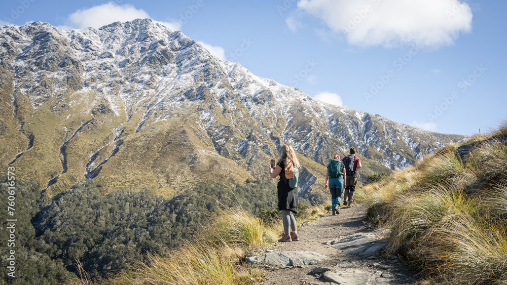 Hikers walking towards snowy mountain during sunny autumn day, New Zealand