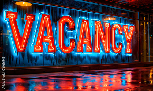 Neon-lit VACANCY sign in bold 3D letters on a reflective blue surface, indicating available employment opportunities or accommodations