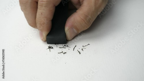 Hand holding black eraser scrap on paper background. 
Error Eraser dust delete wrong words on white background.
top view.   Slow motion.