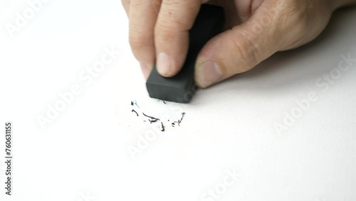 Hand holding black eraser scrap on paper background. 
Error Eraser dust delete wrong words on white background.
top view.   Slow motion.