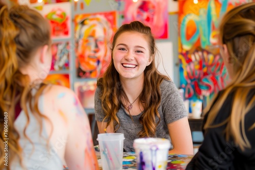 Joyful teenage girl smiling in an art class surrounded by colorful paintings and friends, portraying creativity and happiness.
