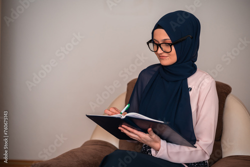 A young Muslim woman in a hijab is studying at home, writing, typing with a pencil on a notebook. photo