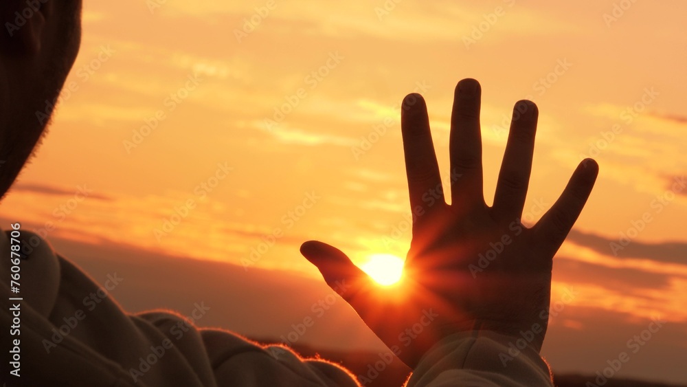 Silhouette of hand at orange sunset. Man stretches hand towards sun, warming palm in summer rays. Unity with nature, enjoyment of trip. Guy gains strength, contemplating, enjoying solitude with nature