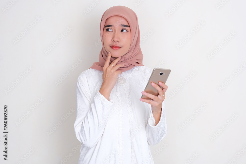 Moslem Asian woman thinking about something while holding mobile phone Moslem Asian woman thinking about something while holding mobile phone
