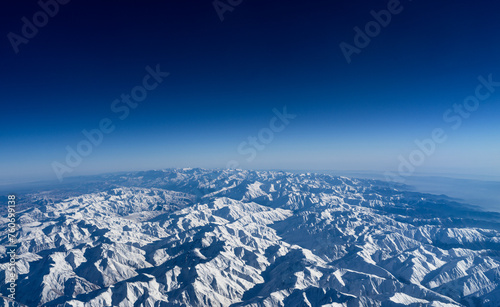 Top of snowy mountain range on blue sky background © Alex