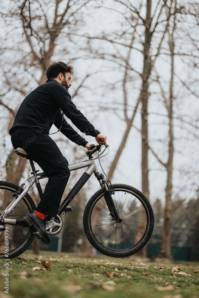 Active man on a casual bike ride in a park with bare trees in autumn.