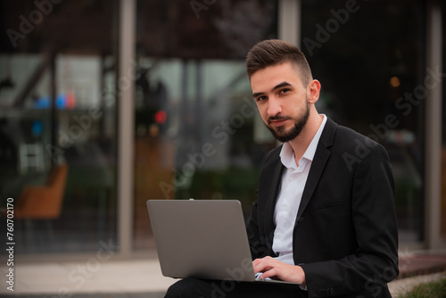 Portrait of a young happy business man using a laptop near the office building