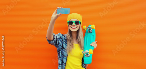 Summer portrait of happy smiling blonde young woman taking selfie with smartphone and skateboard photo