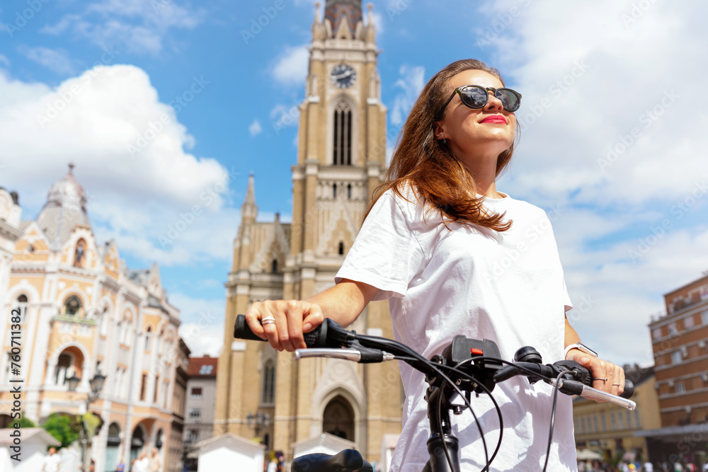 Bike lifestyle in Novi Sad Serbia. Pretty woman stands next to her bicycle on the town square, smiling, enjoying summer.