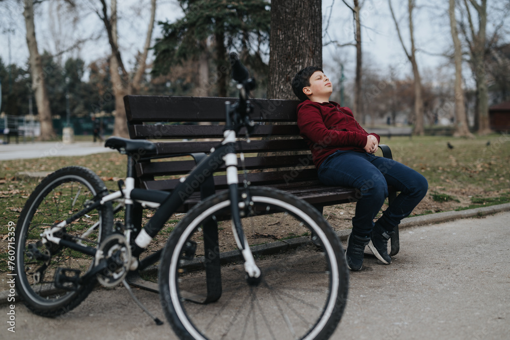 Active young boy takes a break on a park bench next to his bicycle, enjoying the outdoors.
