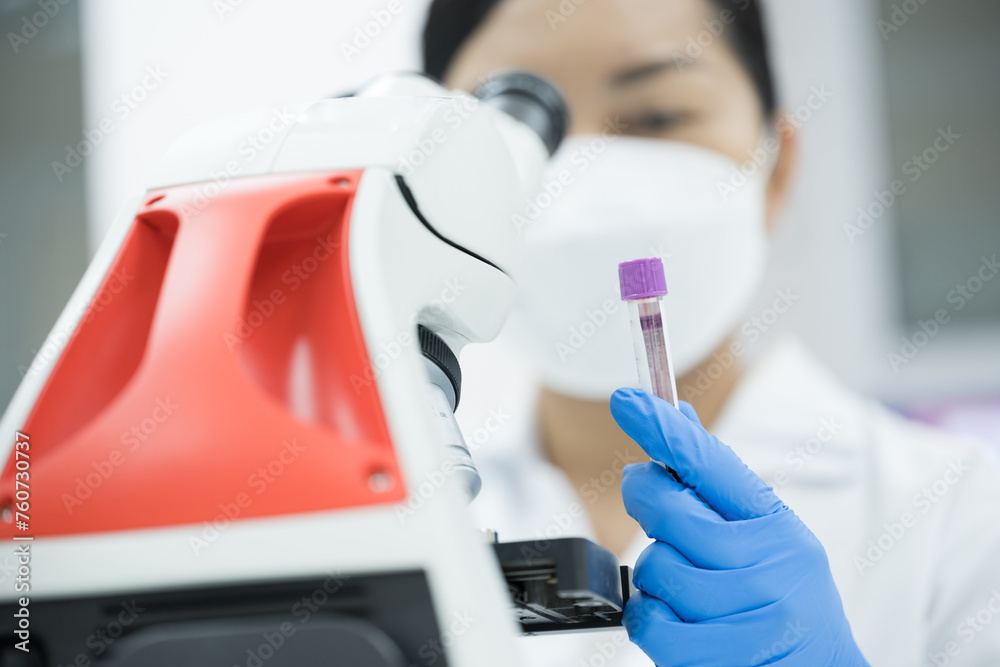 Φωτογραφία Selective focus technician blue glove hand holding blood test tube for scientist diagnosis and blurry microscope at laboratory department in the hospital