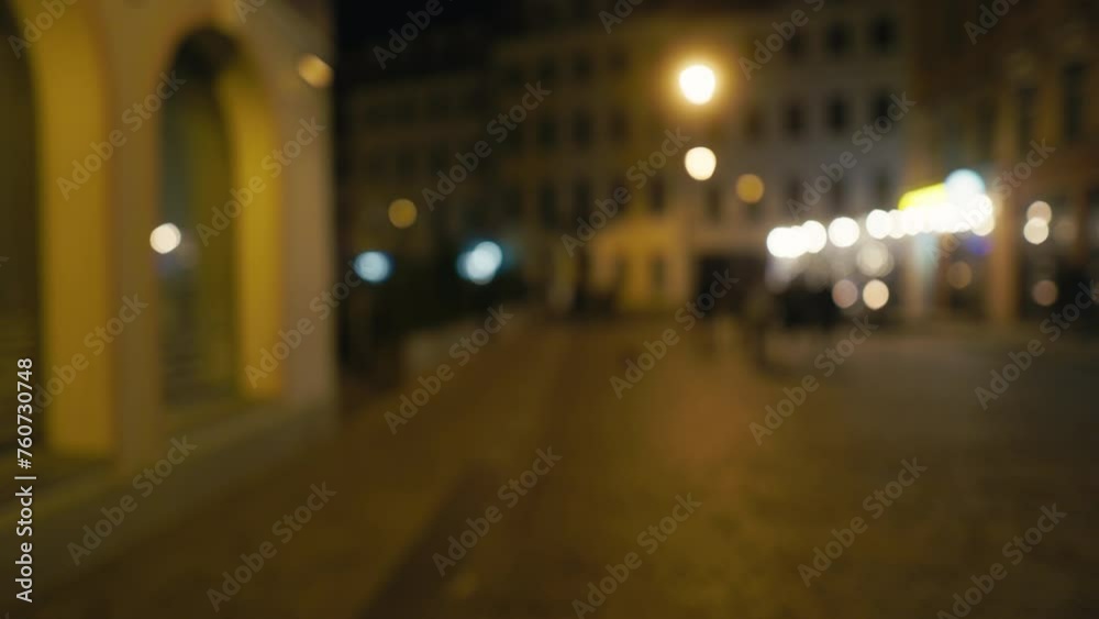 Night view of city street with blurry figures, illuminated by automotive lights