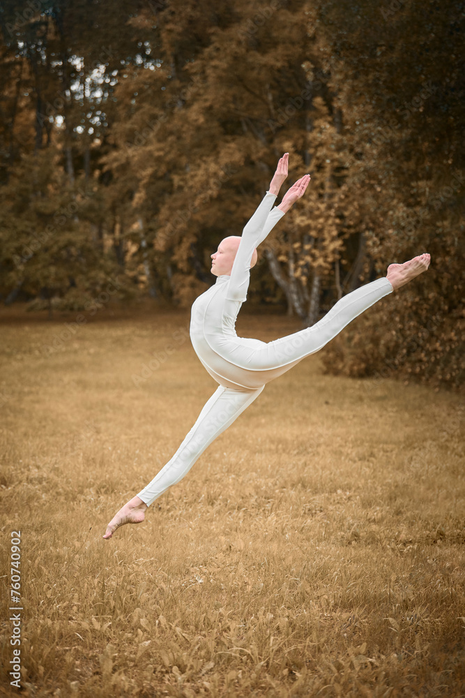 Full length portrait of young hairless girl ballerina with alopecia in tight white suit jumps on fall lawn in park, symbolizing overcoming challenges and gracefully acceptance individuality