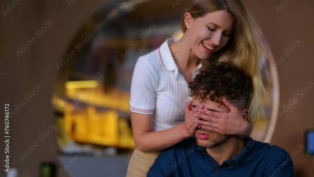 Upset man sitting in restaurant when woman covering his eyes with her hands Upset man sitting in restaurant when woman covering his eyes with her hands