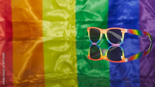 Rainbow sunglasses located on reflective plane and LGBT flag on background