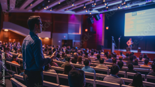 A speaker speaks to attendees in a conference hall who listen with interest