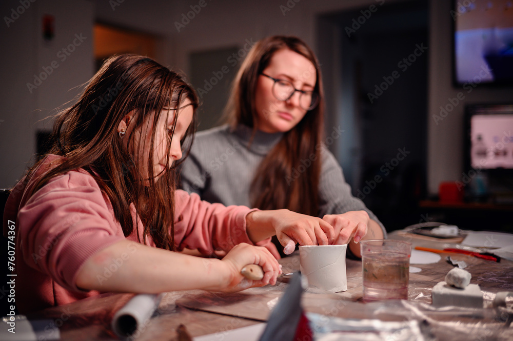Fototapeta premium A girl and a woman are absorbed in creating a craft with clay, a dynamic scene of family interaction and joint creativity at home