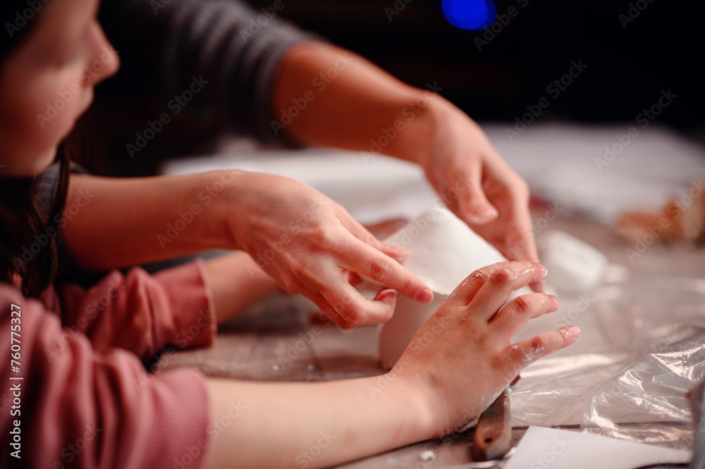 A child's hands carefully construct a clay house, with the focused guidance of a parent, symbolizing the foundational joy of building and learning together