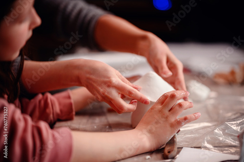 A child s hands carefully construct a clay house  with the focused guidance of a parent  symbolizing the foundational joy of building and learning together