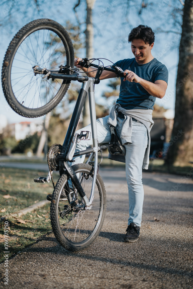 Fototapeta premium A cheerful man enjoys outdoor recreation by lifting his mountain bike in a park with trees in the background.