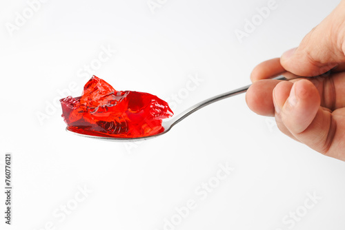 Hand holding a spoon full of red jelly candy isolated on white background