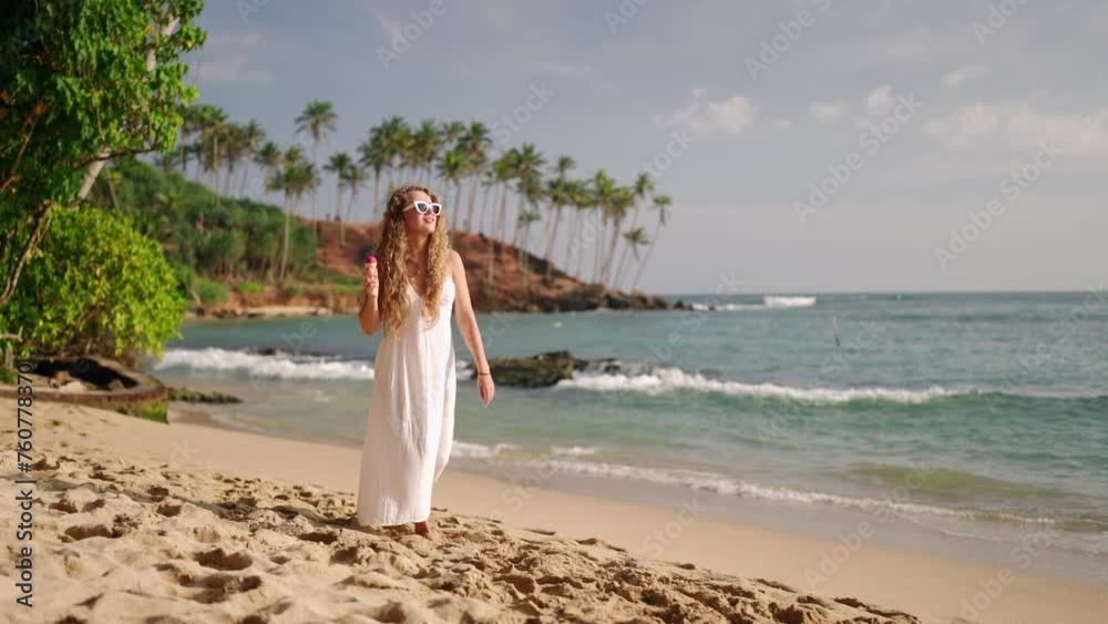 Woman strolls along tropical beach, eating gelato ice cream in sundress. Relaxed stroll on sandy shore, sea breeze. Casual walk enjoying getaway, leisure in coastal paradise with dessert. Slow motion. Woman strolls along tropical beach, eating gelato ice cream in sundress. Relaxed stroll on sandy shore, sea breeze. Casual walk enjoying getaway, leisure in coastal paradise with dessert. Slow motion.