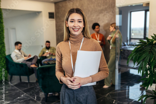 A business woman dressed casually is standing in the lobby of an office building in front of a business team